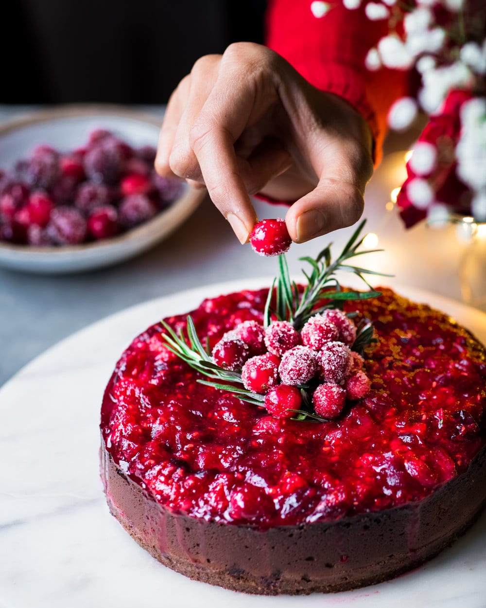 Person placing a cranberry onto cheesecake.
