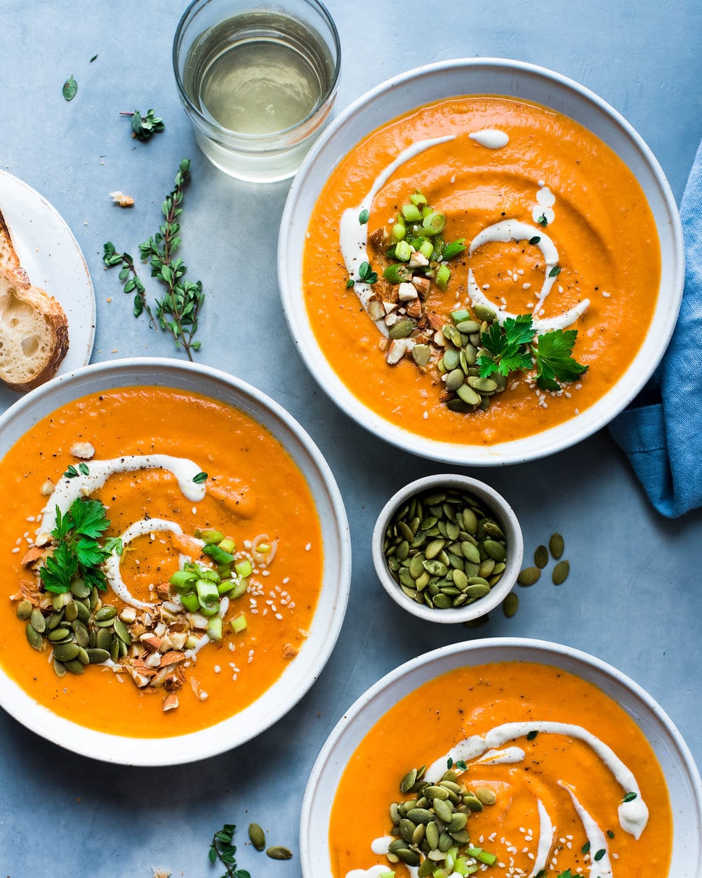 Three bowls of soup and a small bowl of pumpkin seeds on a grey counter.