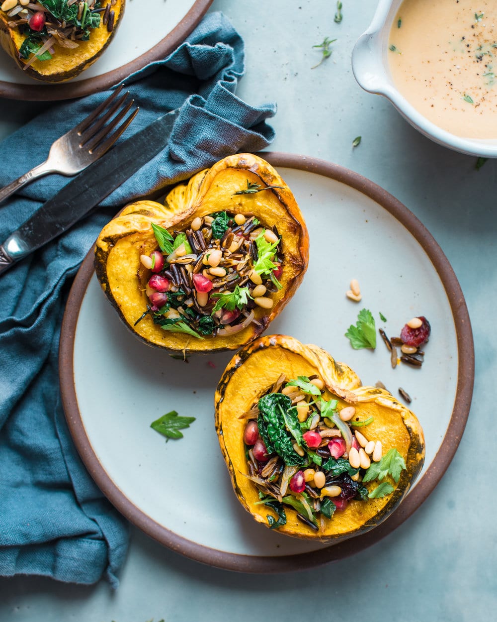 Two roasted squash halves on a plate next to the bowl of tahini sauce on a grey table.