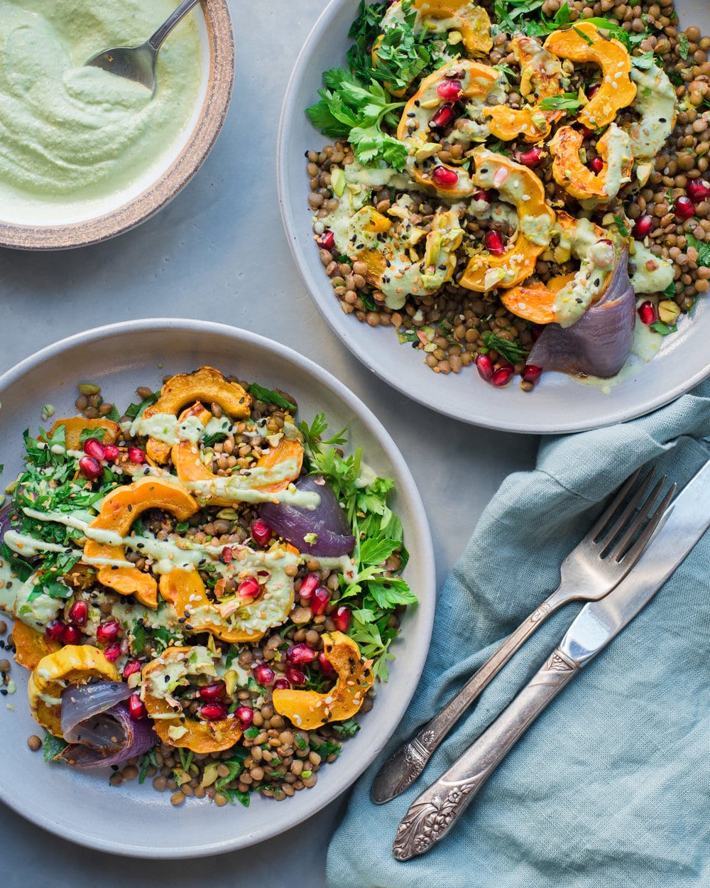 Two large bowls with delicata squash salad and a bowl of cilantro crema on grey table.