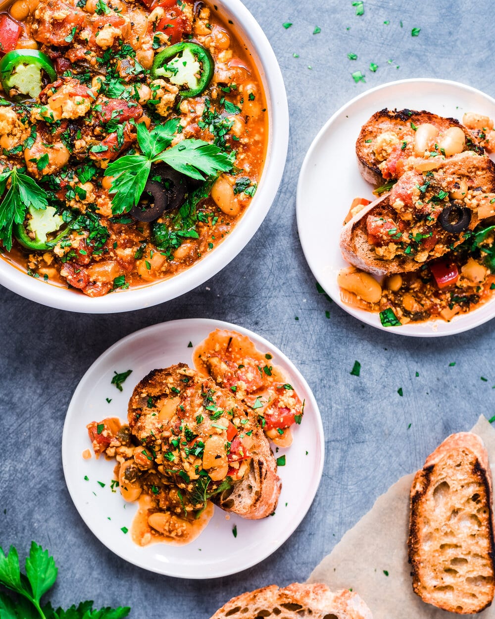 Two plates of shakshuka on toast next to one large serving plate.