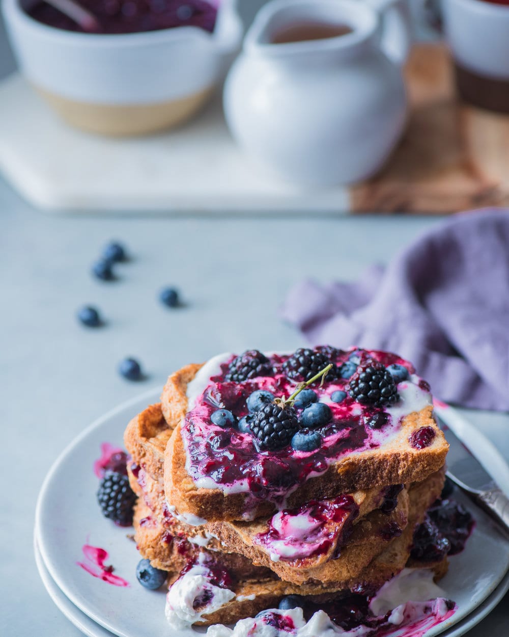 Stack of berry french toast on two white plates on a white table.