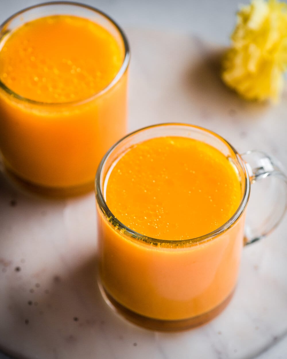 Two glass mugs filled with turmeric tonic on a marble serving board.