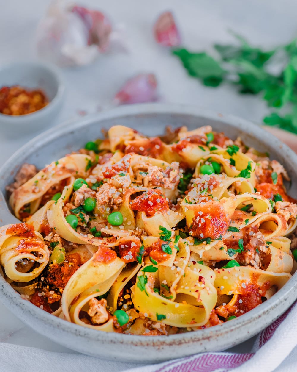 Pappardelle noodles in bolognese sauce in white bowl on white table.