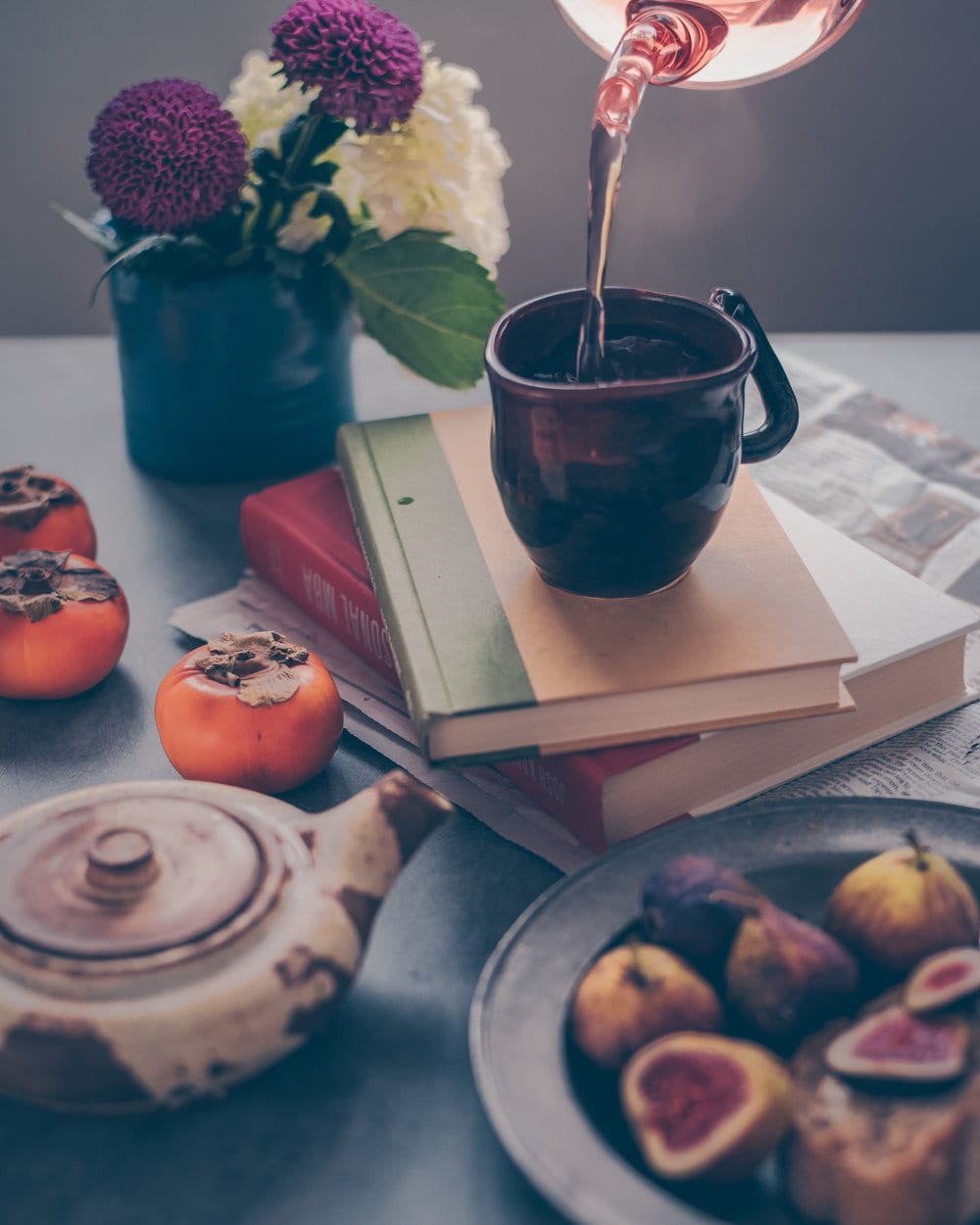 Tea being poured into a mug sitting on a stack of two books on a table.