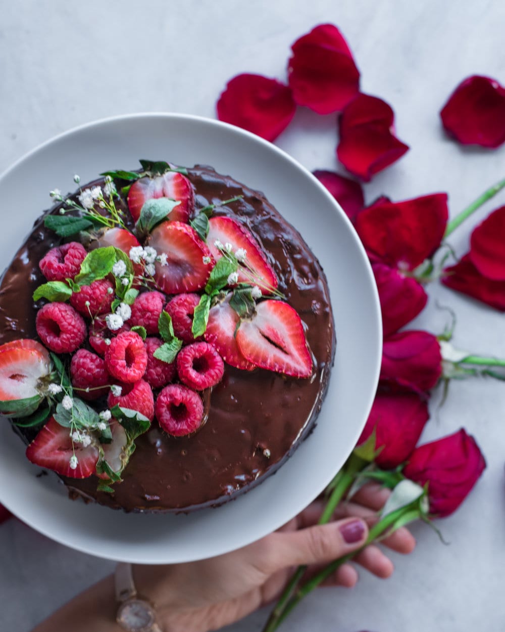 Chocolate Cake with berries on white plate on a white table with rose petals.