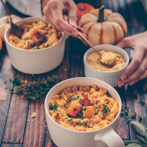 woman's hands holding mug of butternut squash risotto on a table.