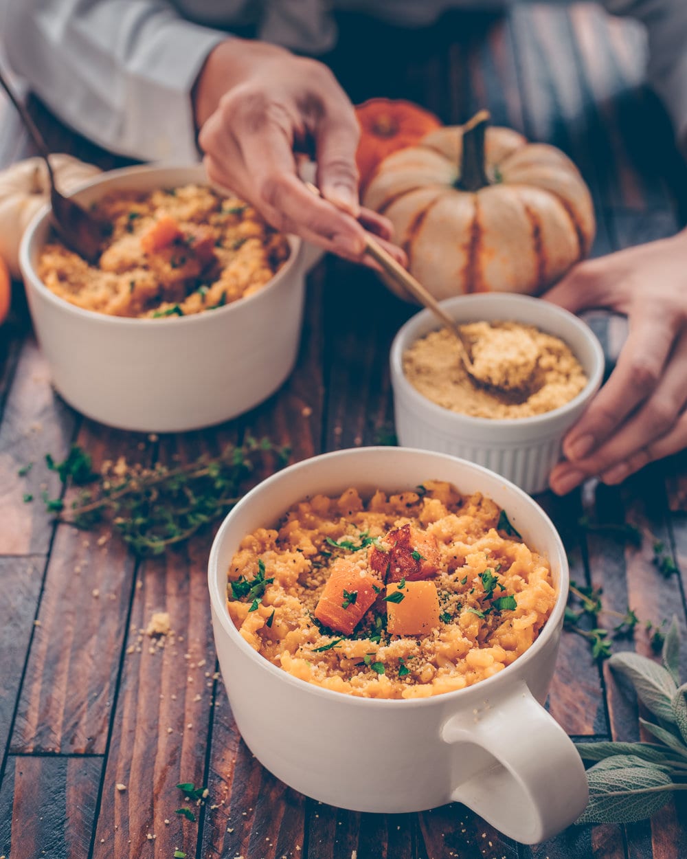 woman's hands holding mug of butternut squash risotto on a table.