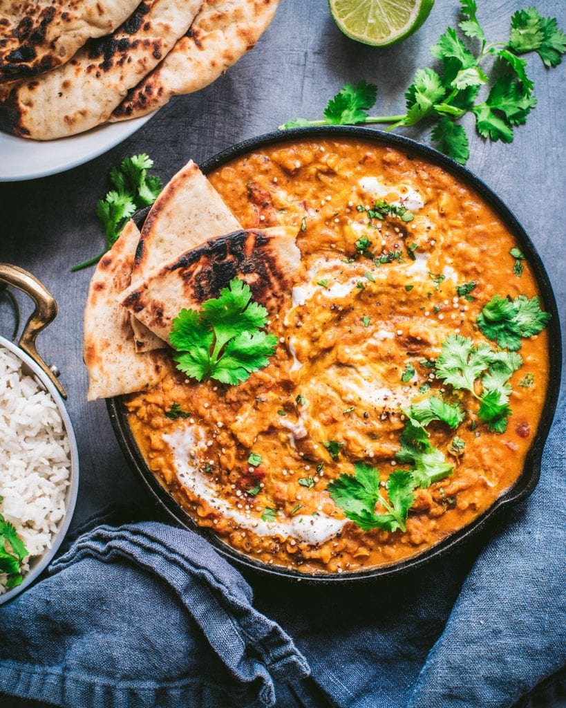 skillet with vegan red lentil curry, topped with cilantro and served with naan