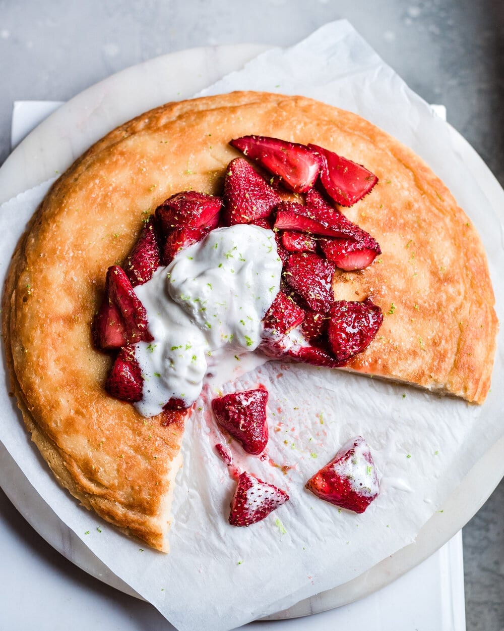 Strawberry dutch baby on parchment paper with ice cream and lime zest with a slice taken out.