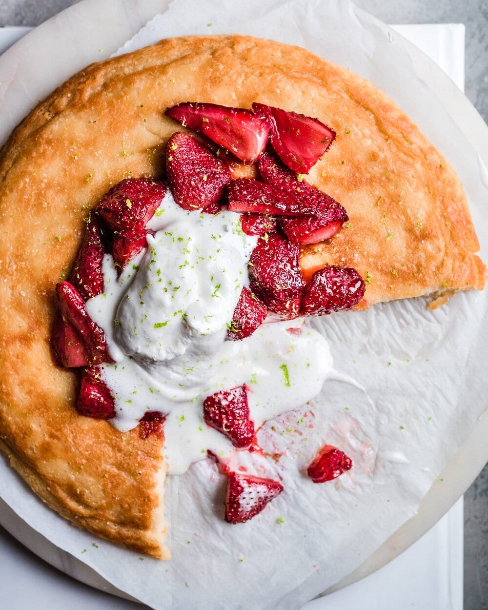 Dutch baby with strawberries and ice cream on parchment paper with one third cut out of it.