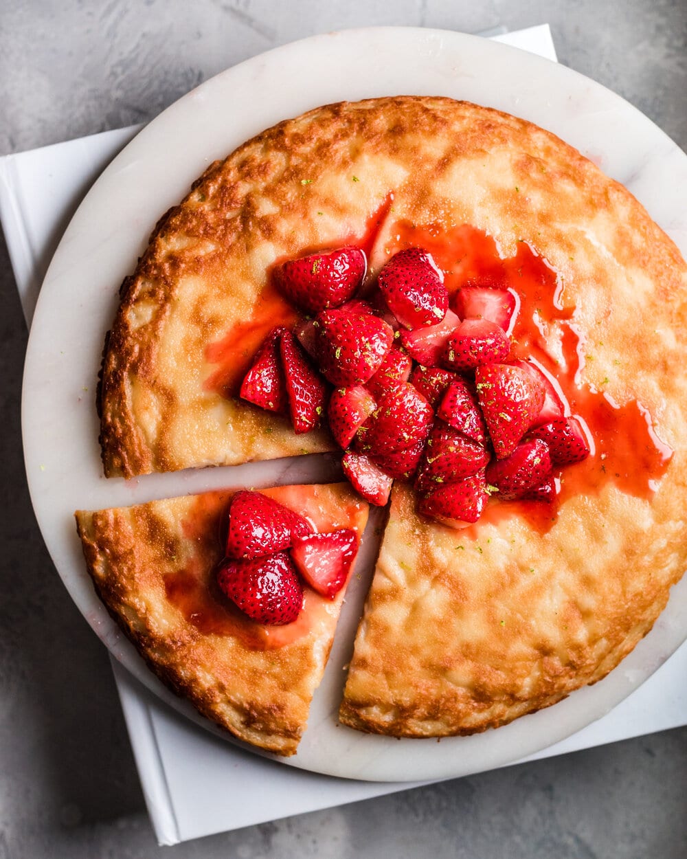 Slice cut out of dutch baby with strawberries on marble board.