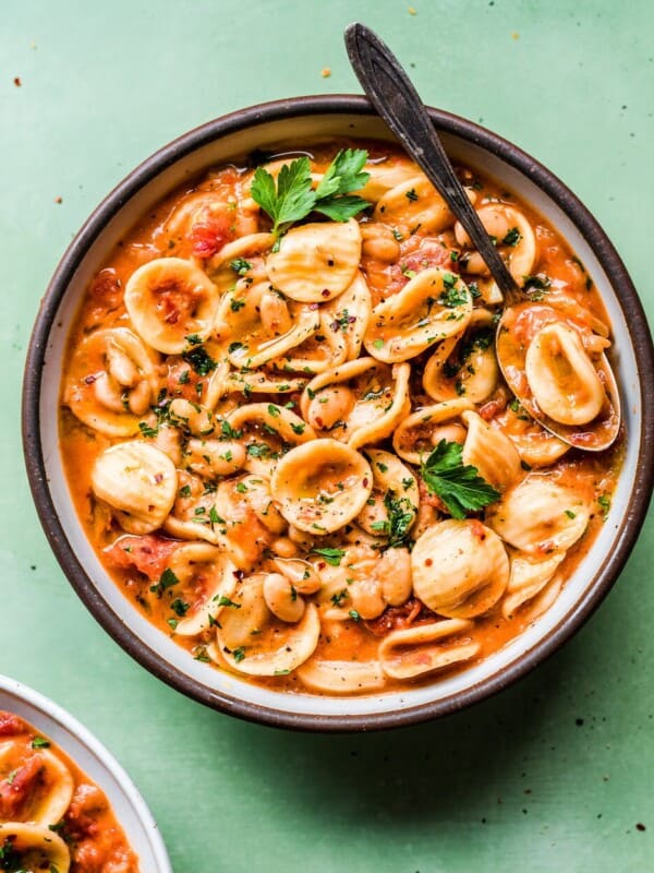 italian pasta and white bean stew in a ceramic bowl on a green surface.