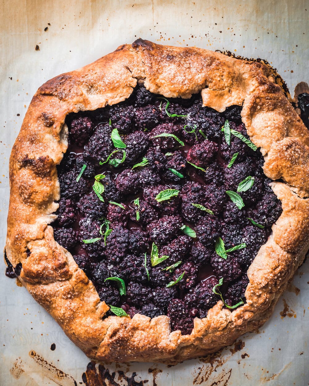 Cooked blackberry galette with mint and basil on a baking sheet.
