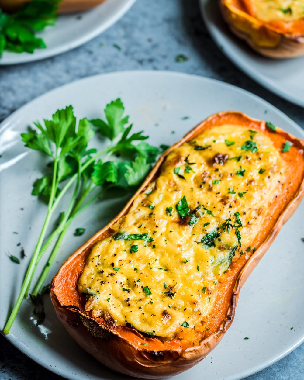 Stuffed butternut squash on a large plate with stalks of parsley.