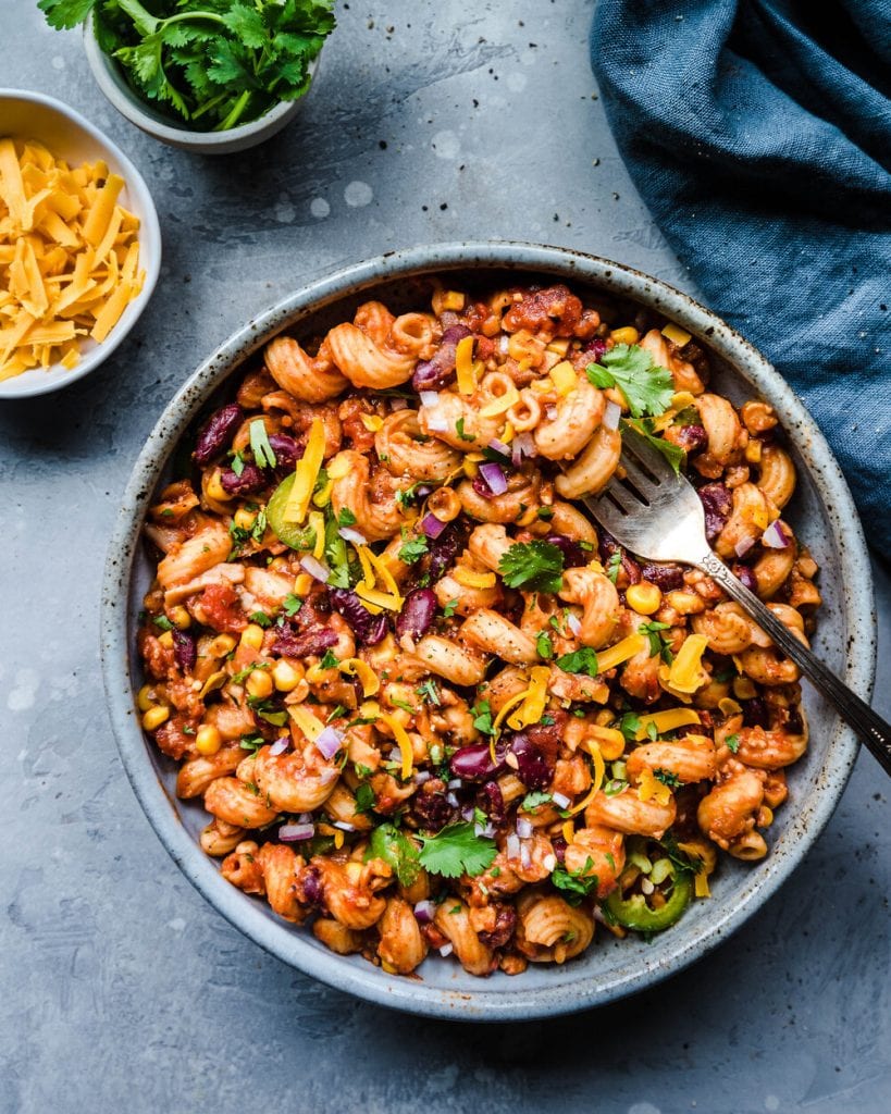 bowl of vegan chili mac with fork, and vegan cheese and cilantro