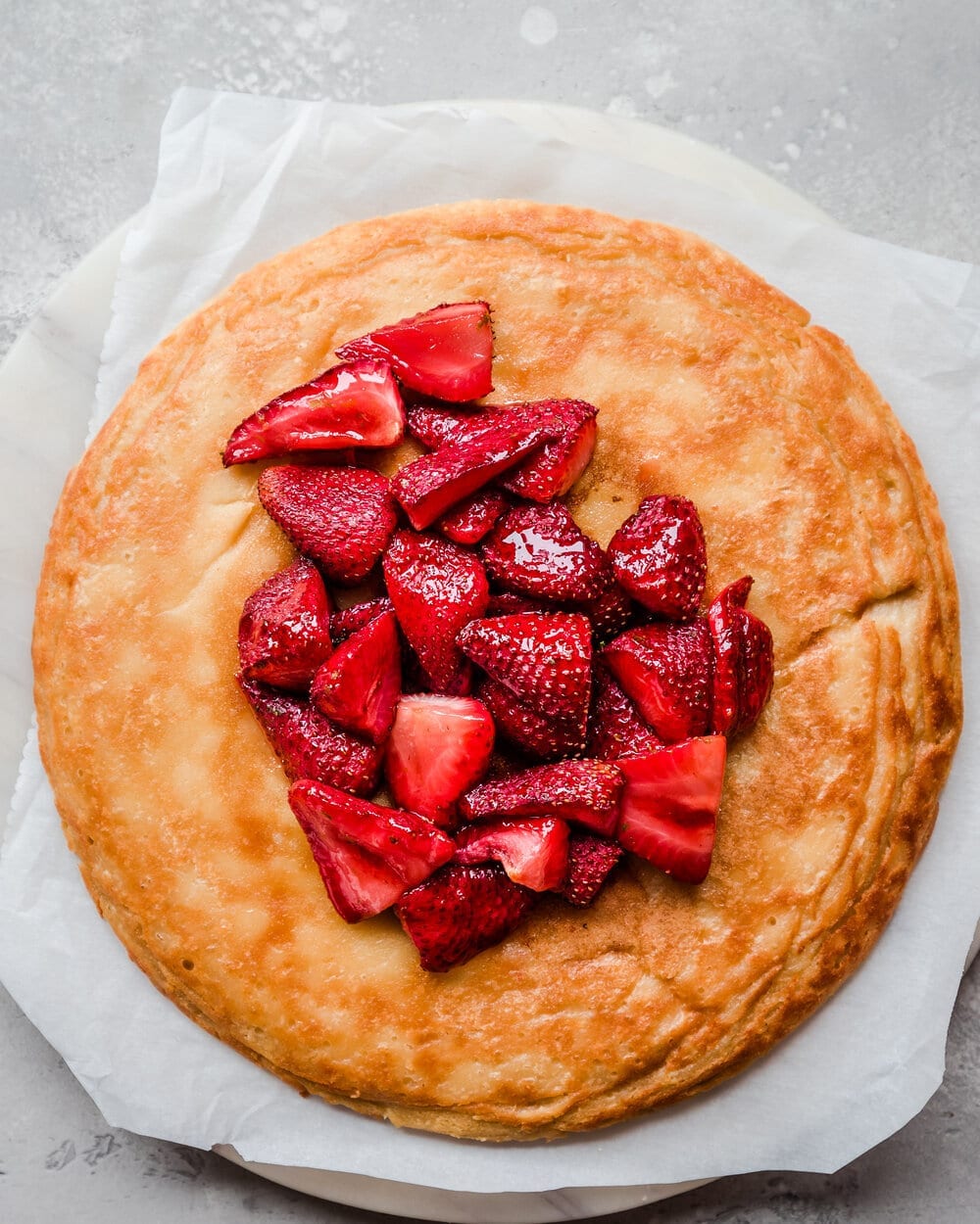 Dutch baby with strawberries on parchment paper on white table.