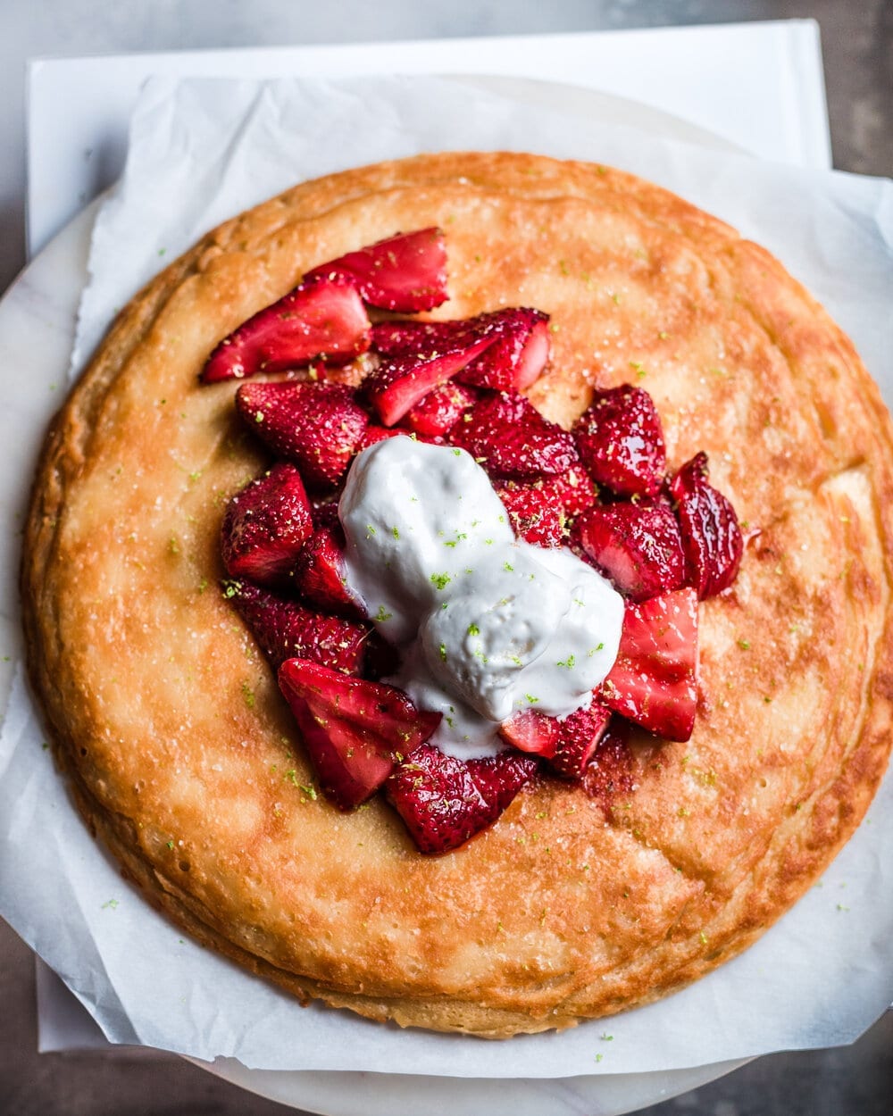 Strawberry dutch baby on parchment paper with ice cream and lime zest.