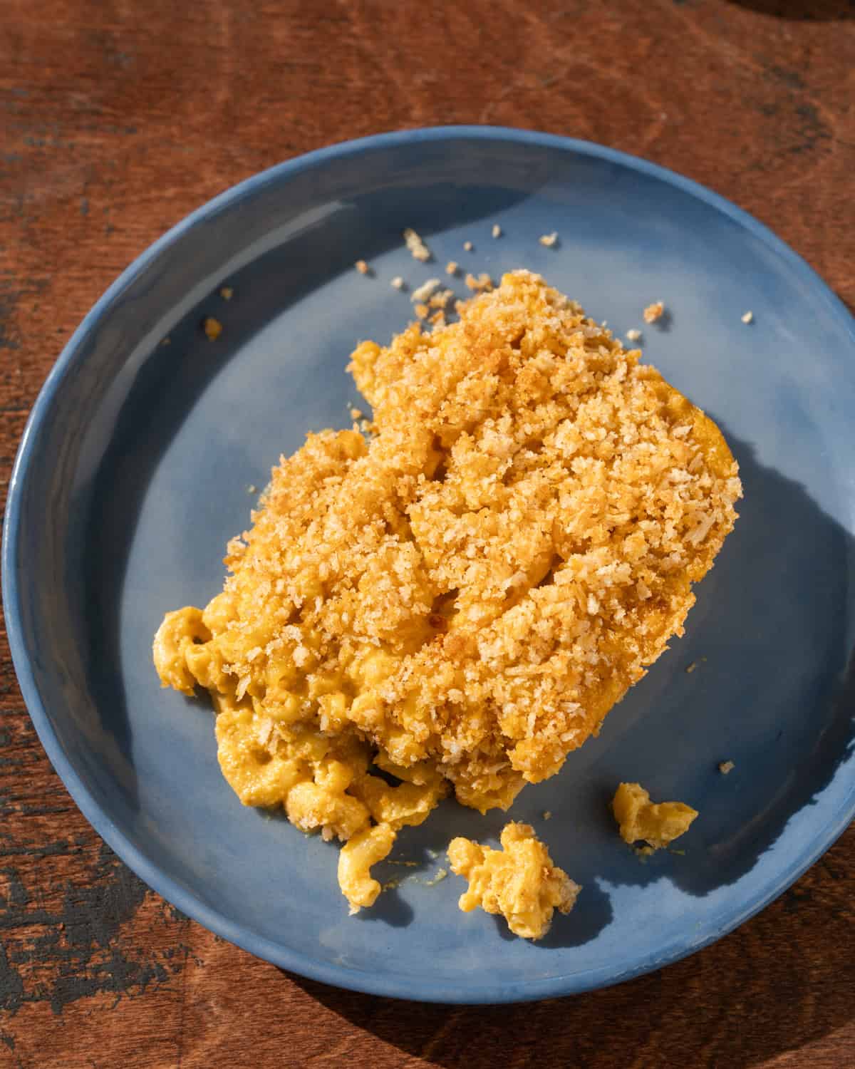 a big slice of baked vegan mac and cheese on a blue plate on a wooden table.