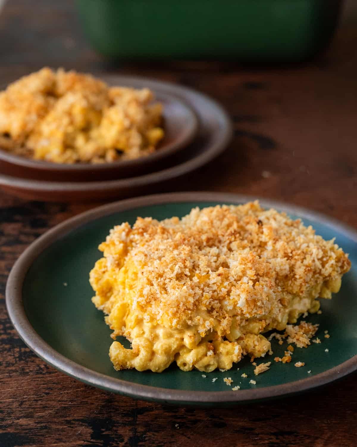 a gooey slice of vegan mac and cheese with crispy topping on a green plate.
