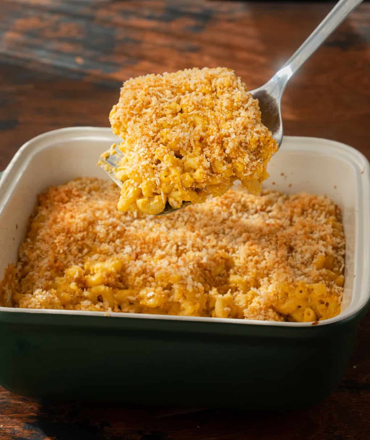Spatula lifting a slice of crispy baked mac and cheese out of a ceramic casserole pan.
