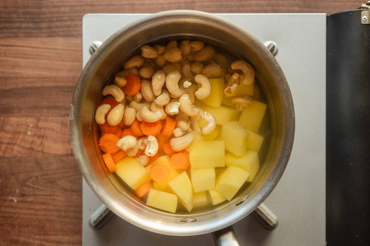 sliced carrots, sliced potatoes, and cashews in a saucepan covered with water.