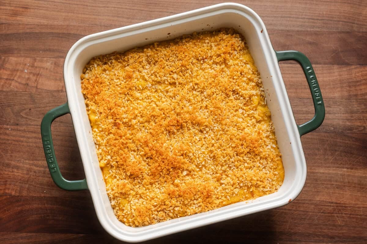 crispy baked vegan mac and cheese in a ceramic baking dish on wooden table.