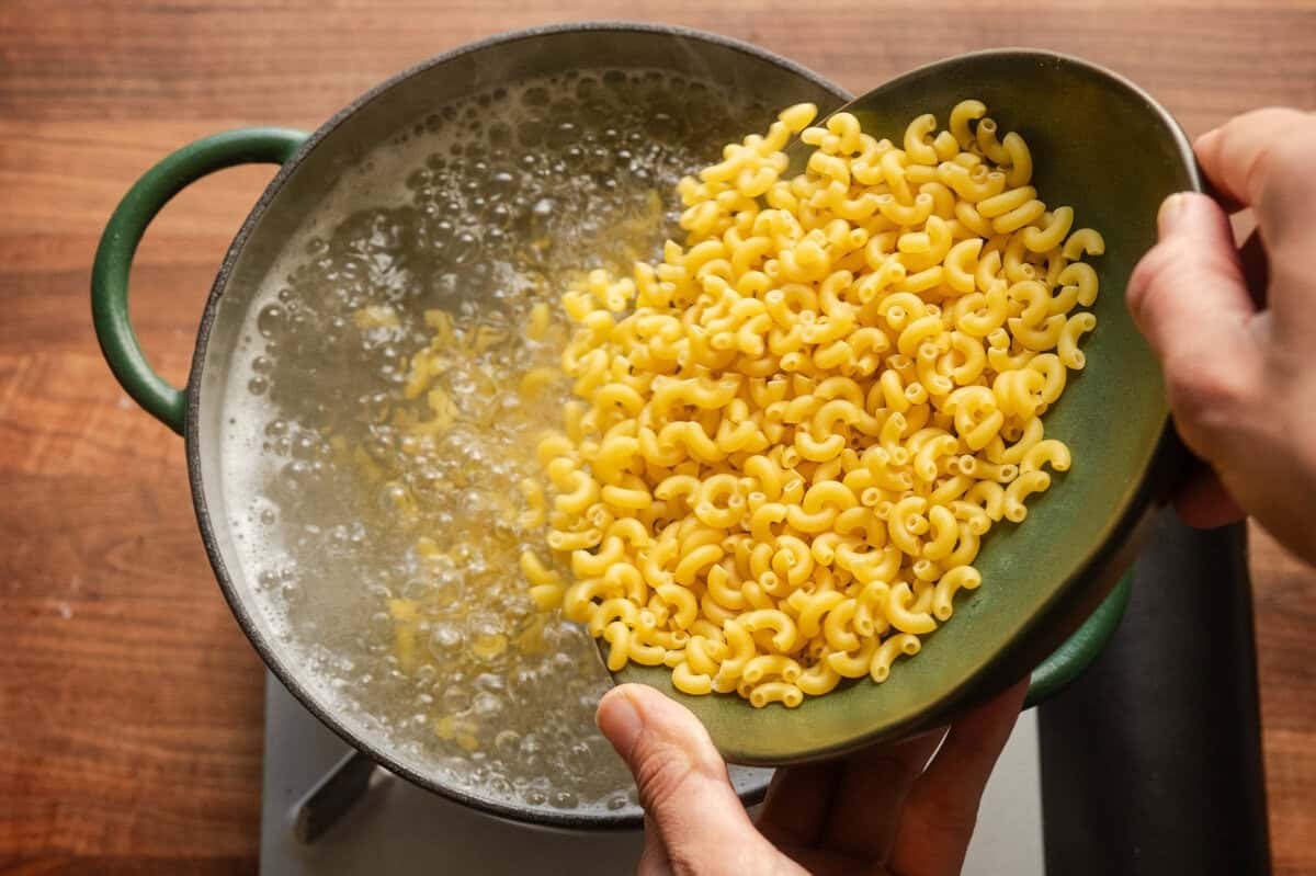 adding elbow macaroni to a green saucepan of boiling water.