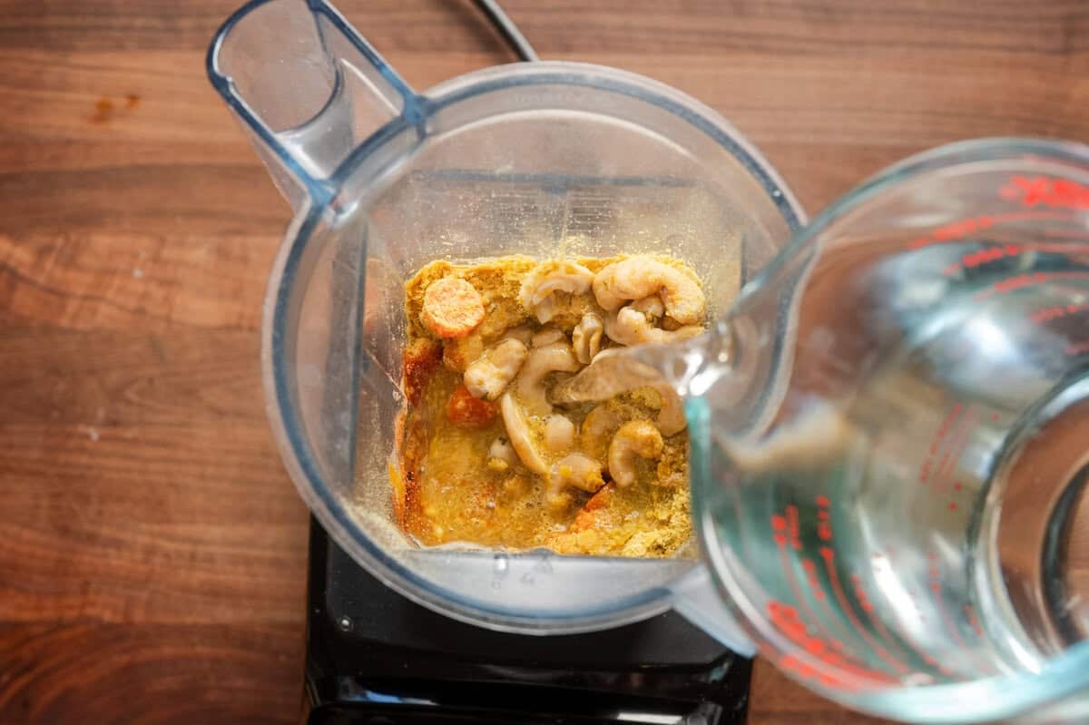 pouring water into a blender with cashews, carrots, and spices.