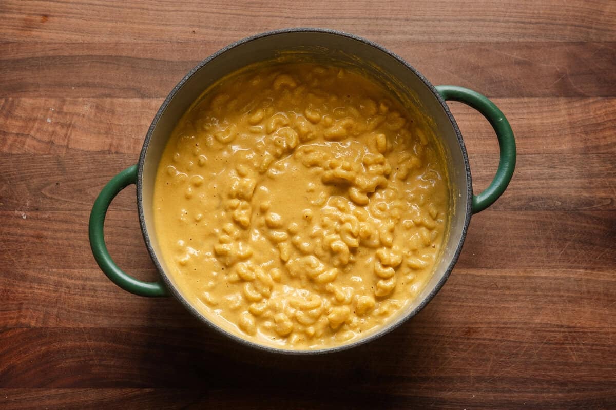 creamy vegan mac and cheese in a green saucepan on a wooden table.
