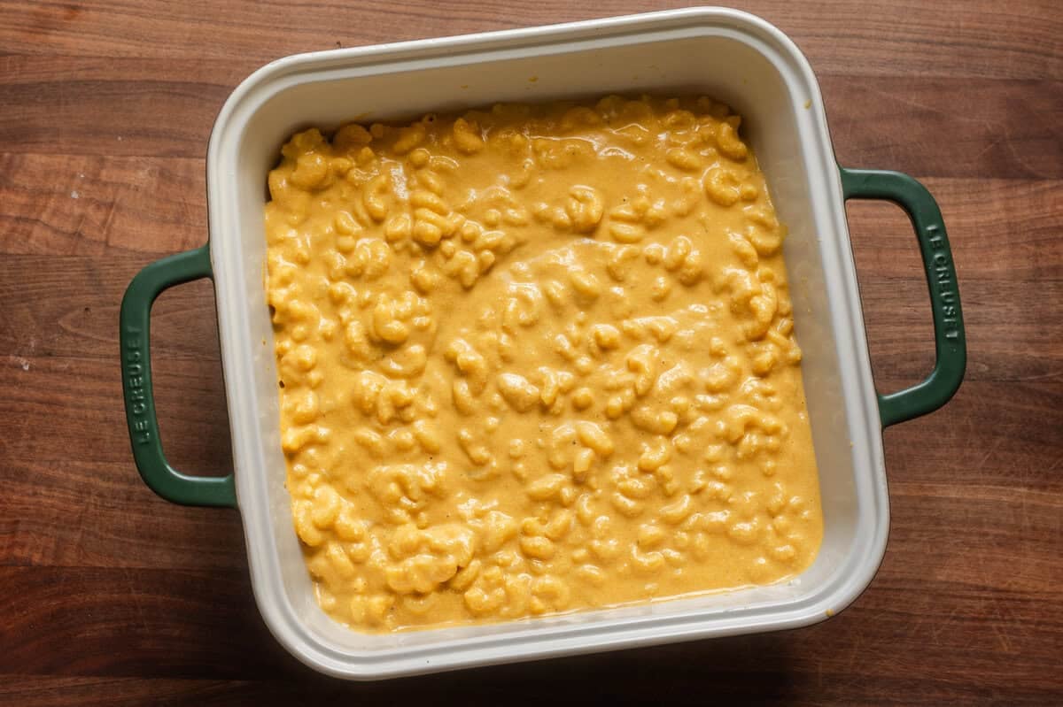 saucy vegan mac and cheese in a ceramic baking dish on wooden table.