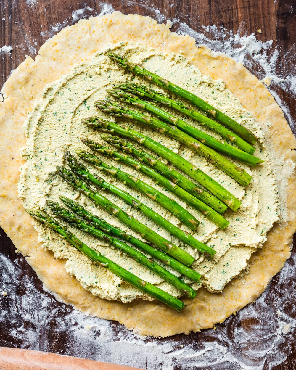 Tofu ricotta and asparagus on galette dough on a wooden cutting board.