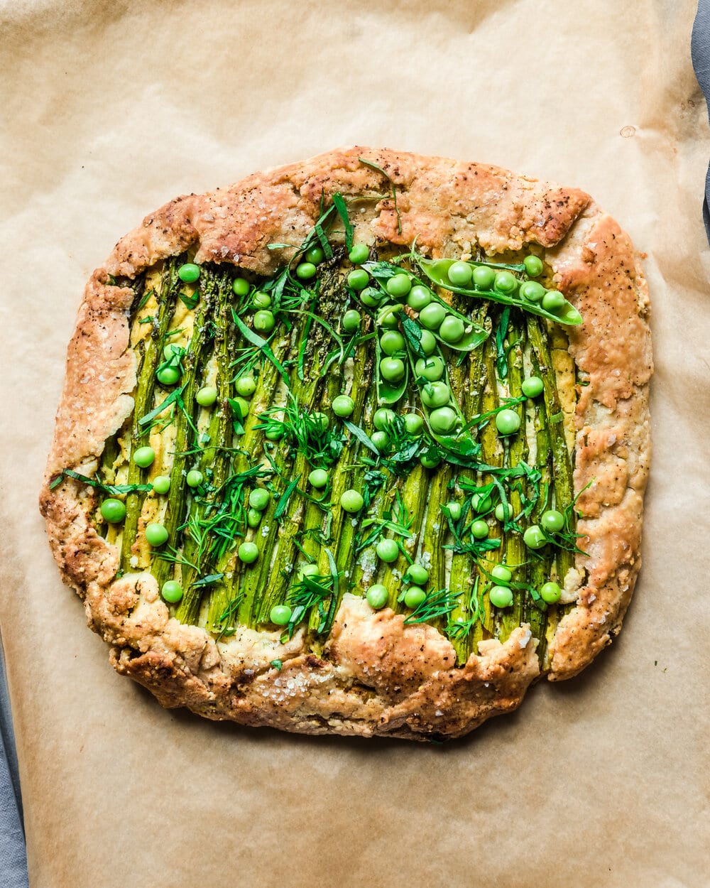 Cooked galette with fresh peas on a piece of parchment paper.