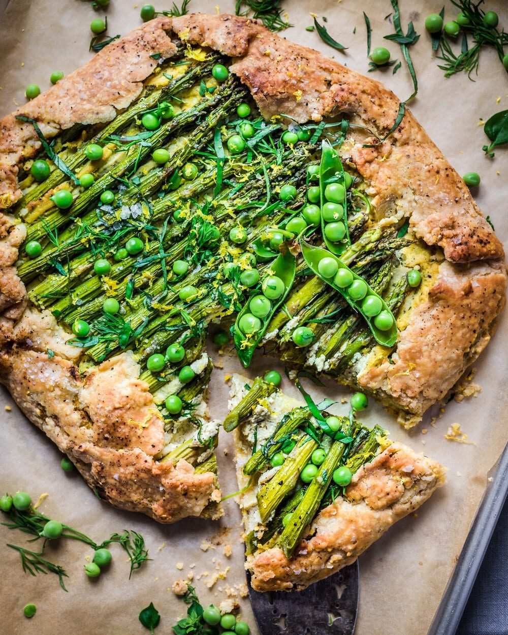 Baked asparagus galette with a slice cut from it on a piece of parchment paper.