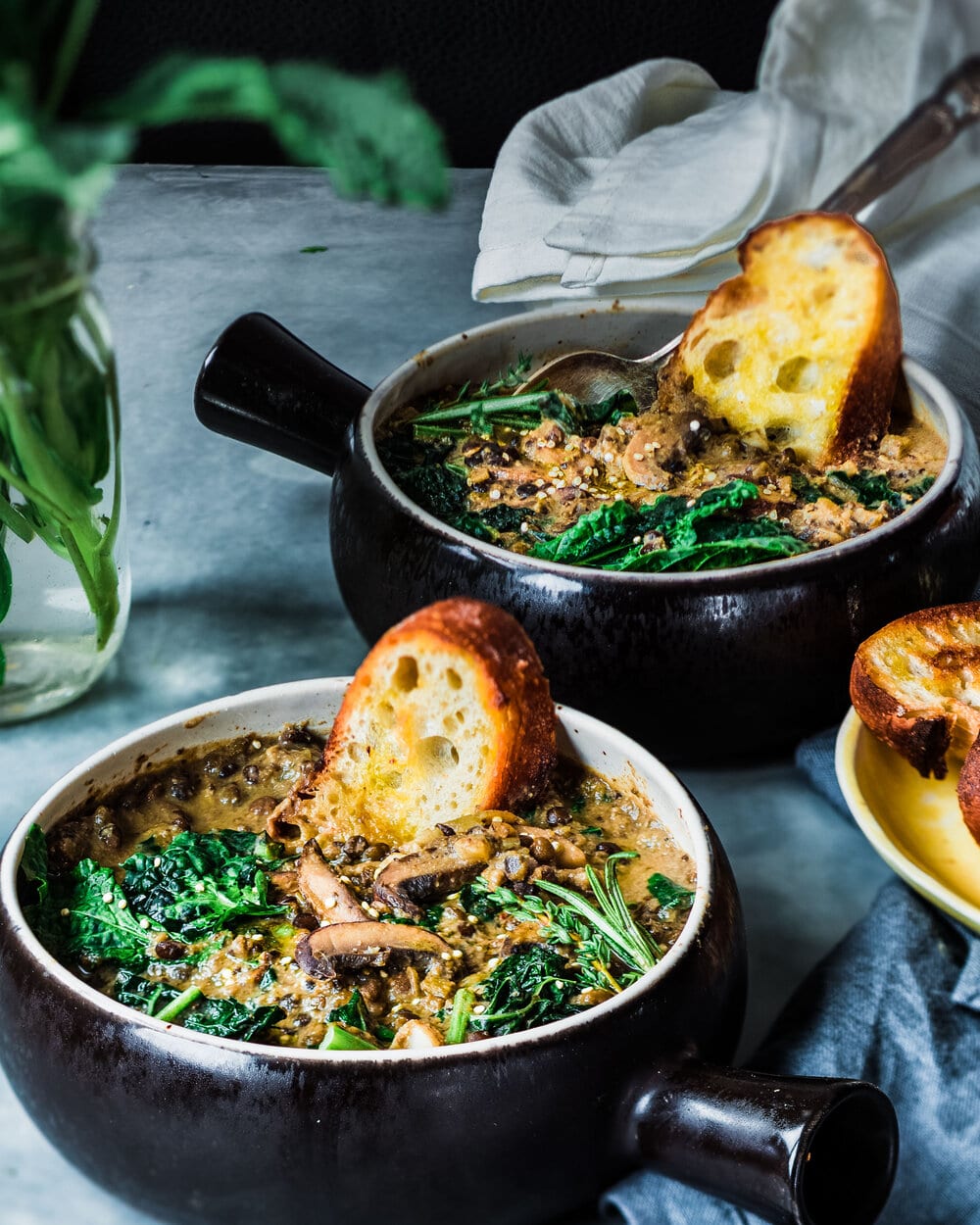 Two bowls of lentil stew with bread on a table.