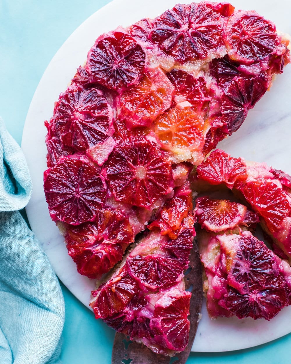 Blood orange cake cut in half and in slices on a white marble serving board.