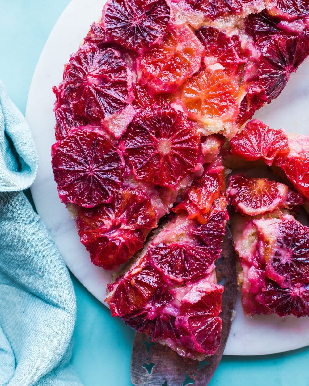 Blood orange cake cut into half and in slices on a white marble serving board.