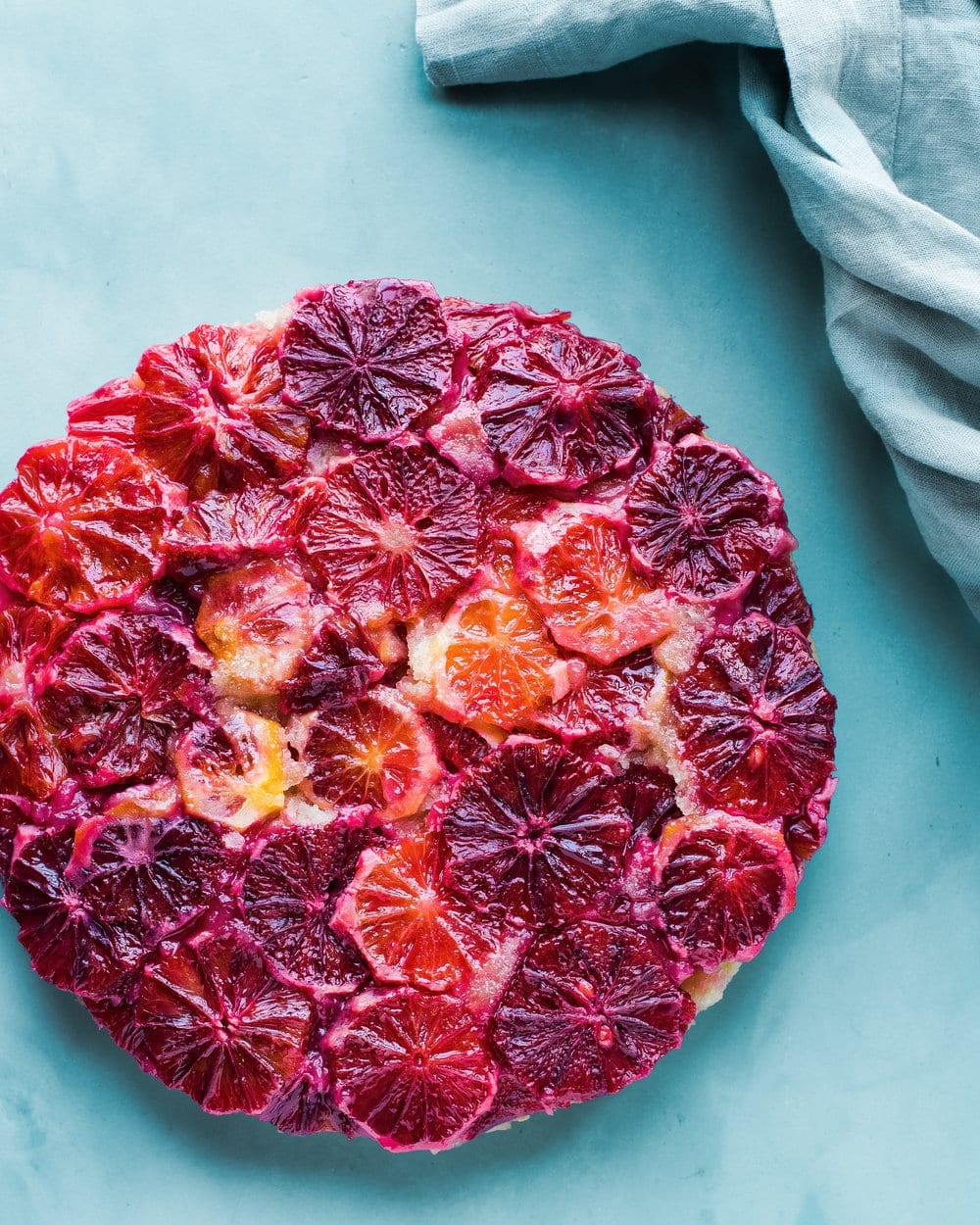 Full blood orange cake on a blue table.