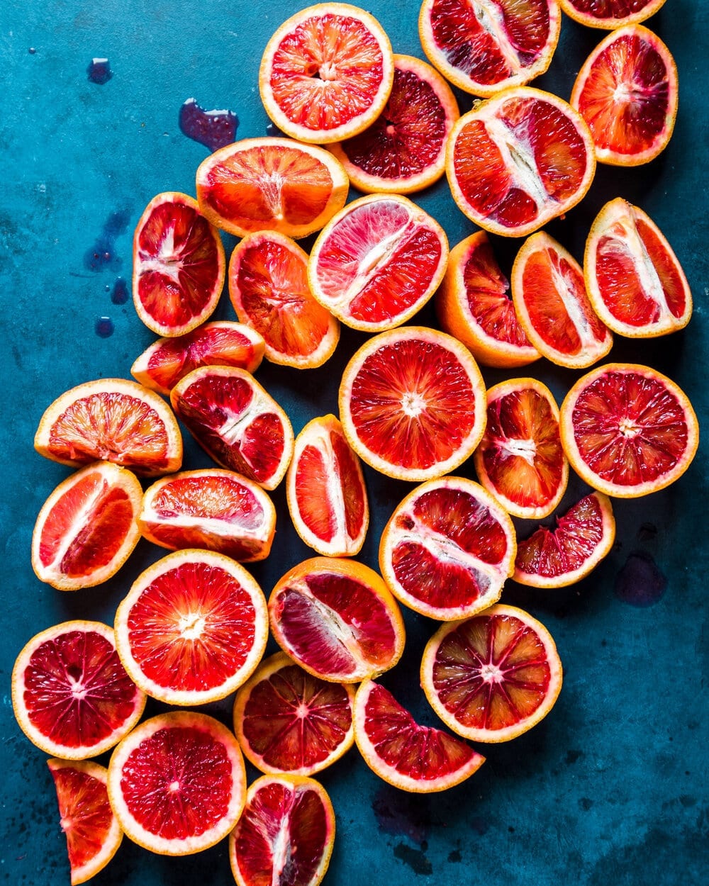 Blood orange halves and quarters on a dark blue table.