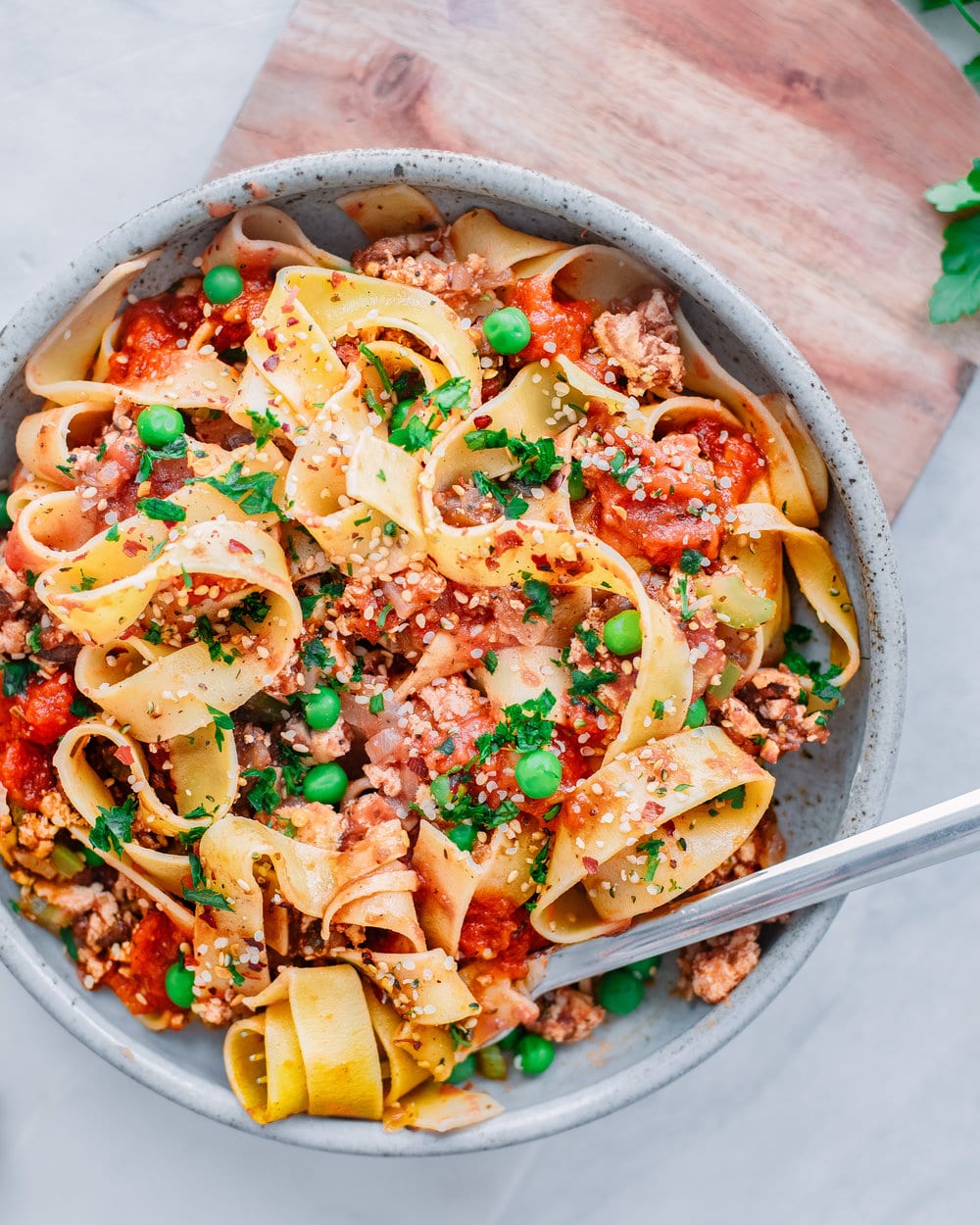 Overhead photo of pappardelle bolognese in a bowl with a fork on white table.