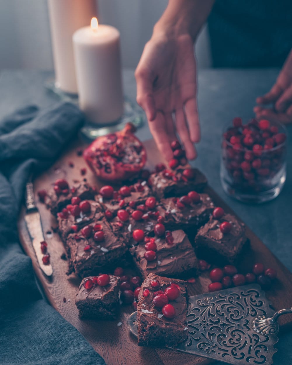 Hand dropping cranberries onto brownies on a wooden cutting board.