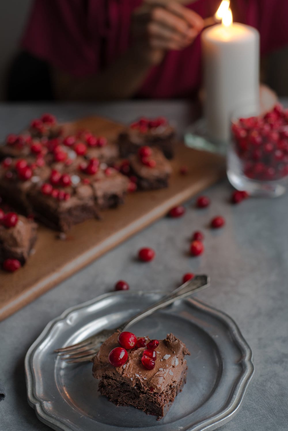 A brownie on a silver plate in front of a woman lighting a candle. 