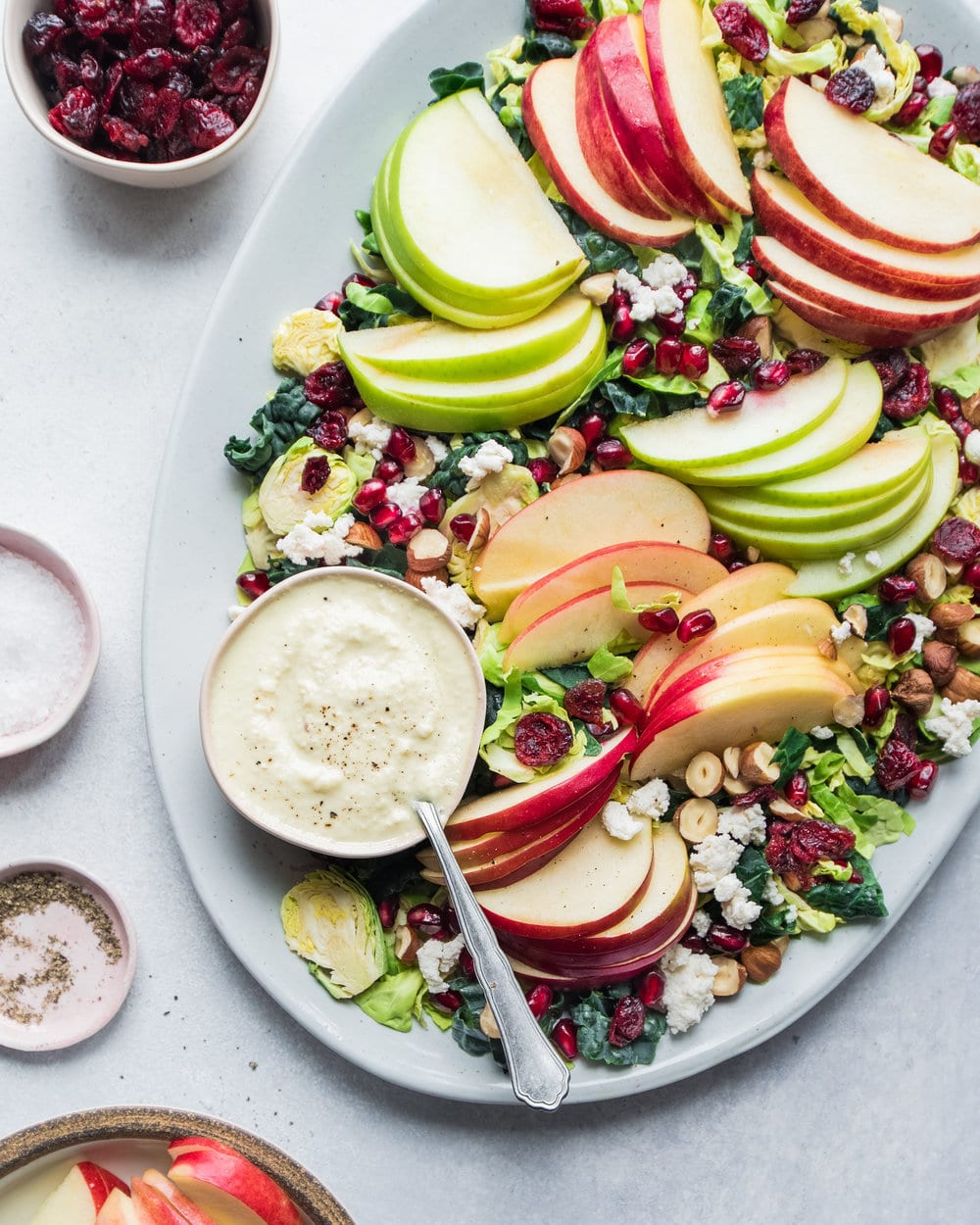 Kale salad with sliced apples, pomegranates, avocado and dressing on a large white platter.