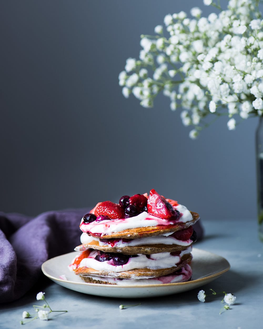 Stack of pancakes with yogurt and berries on a grey plate.