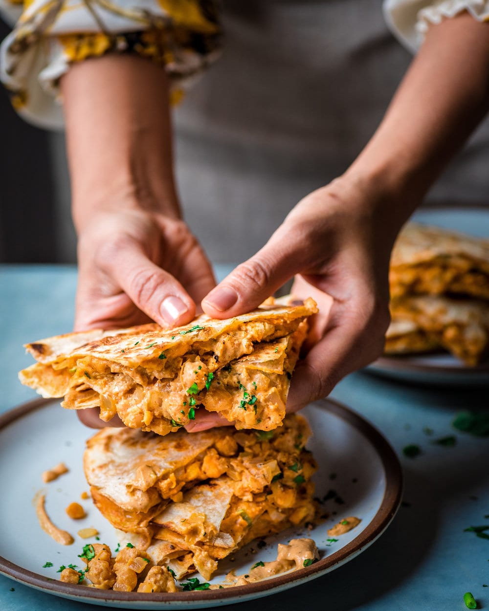 Woman holding a quarter of a buffalo chickpea quesadila over a plate with the rest of the quesadilla.