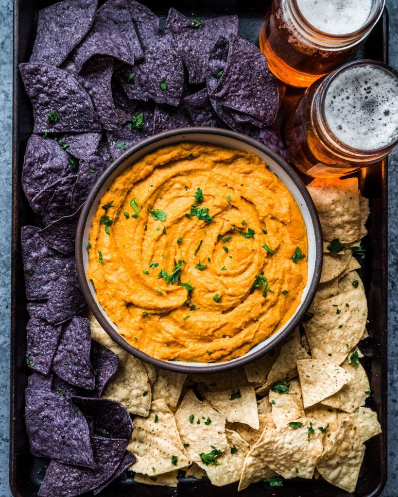 Cheesy Buffalo Cauliflower Dip in a bowl surrounded by tortilla chips and beers