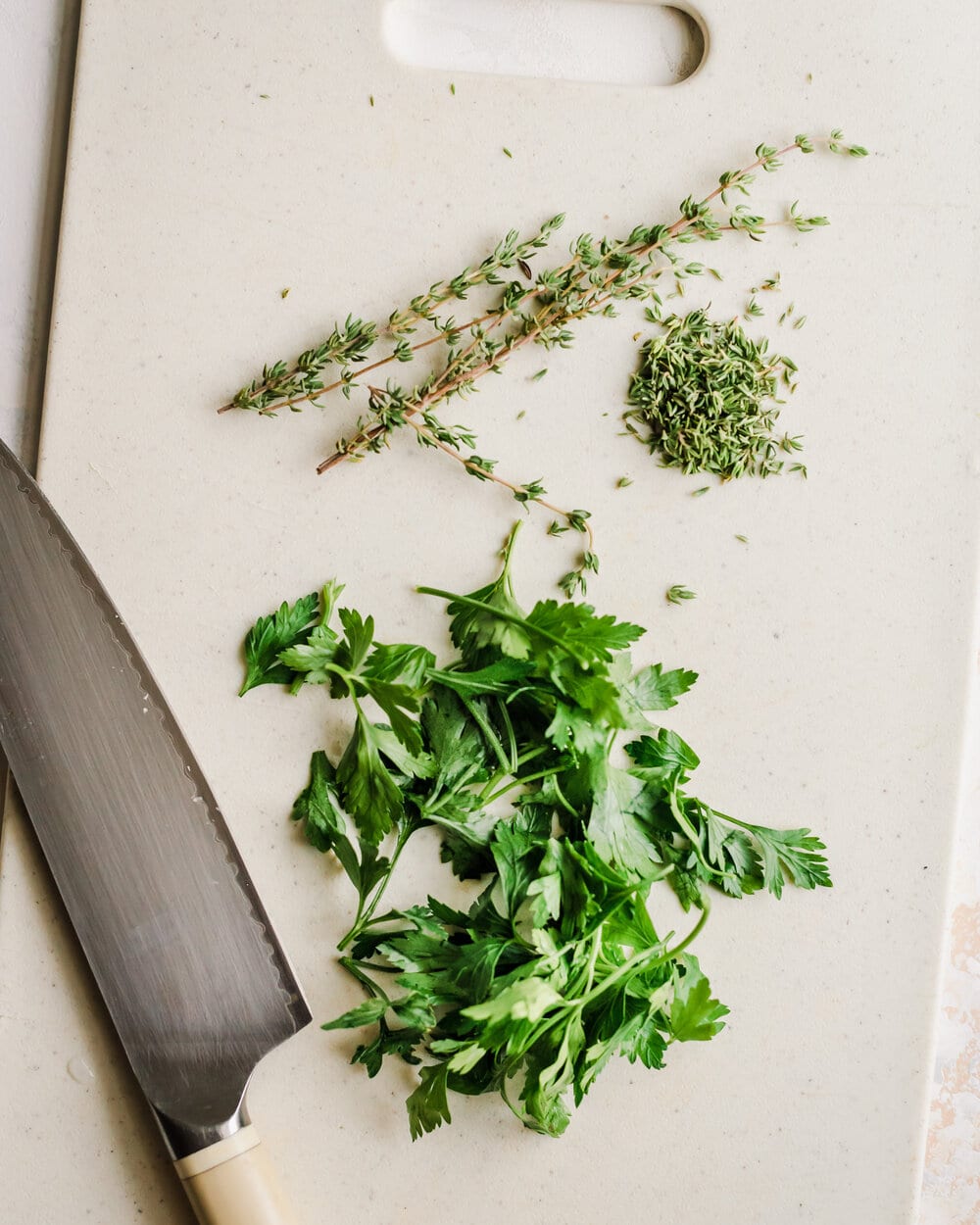 parsley and thyme on a white cutting board with knife. 