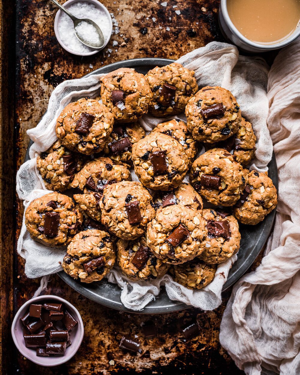 A platter of vegan chocolate chunk cookies in a metal tin with a cloth napkin.