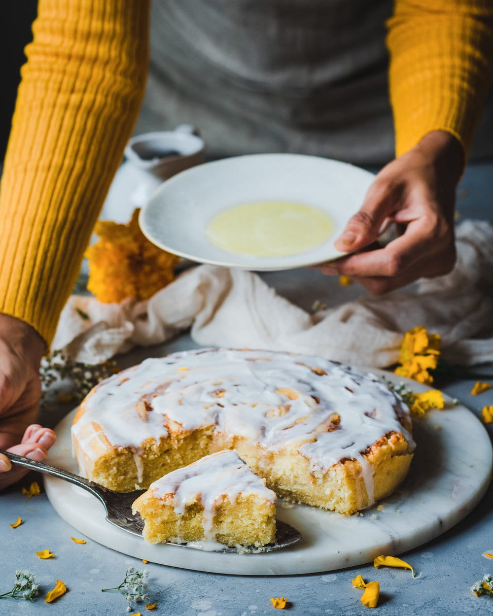 Woman using cake server to take a piece of cake from marble serving board.