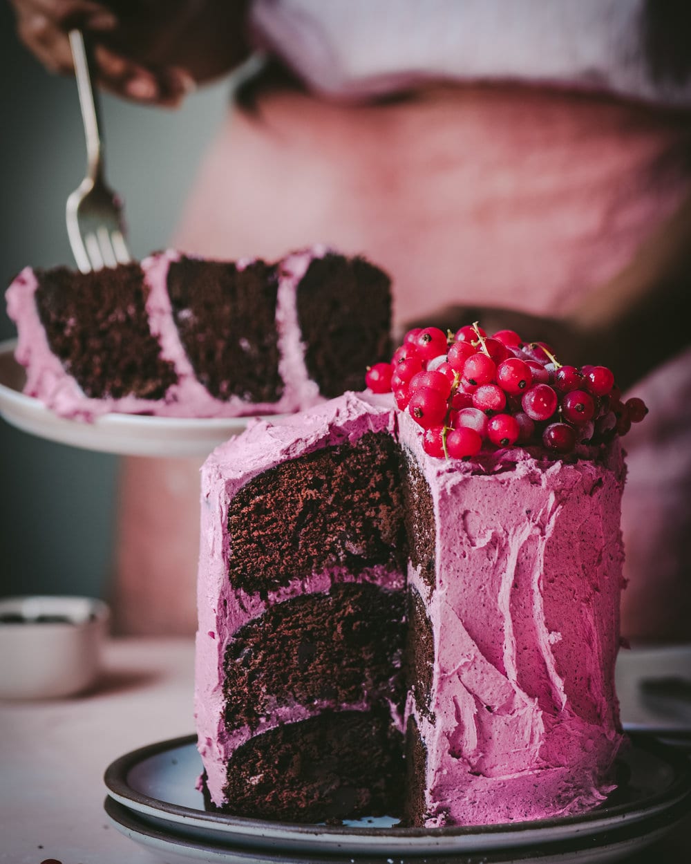 Woman digging into a slice of cake on a plate behind the cake on table.